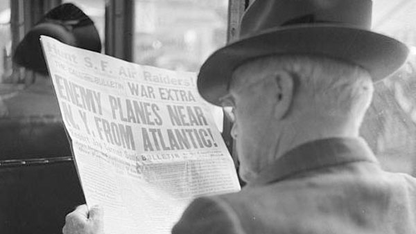 a photograph of a man reading a 1941 newspaper with the headline “Enemy Planes Near N.Y. from Atlantic”