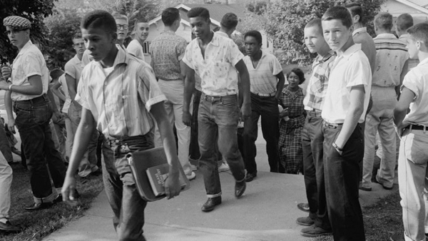 black and white photograph of African-American teenage boys heading to school, while being watched by a group of white teen boys