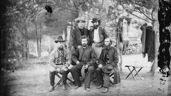 black and white photo of five men posing for a photo in a clearing in the woods