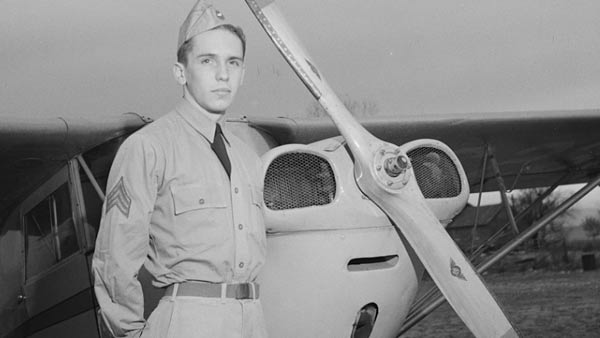 black and white photo of a man in uniform standing in front of a small propeller plane