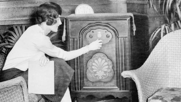 black and white photo of a woman turning on a large radio