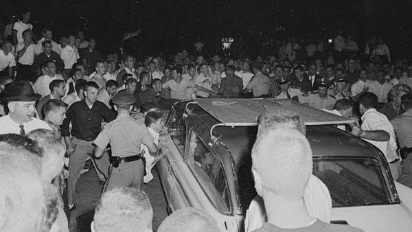 black and white photo of a large mob of people surrounding a car