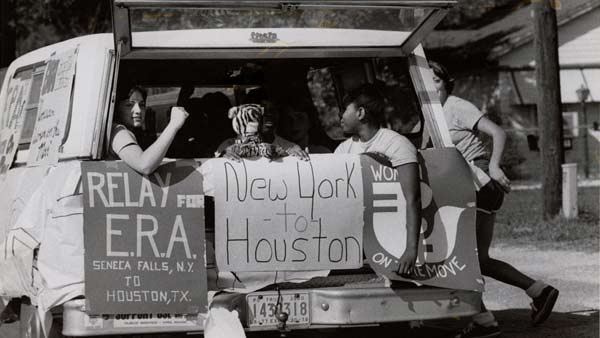 black and white photo of women in the back of a station wagon holding signs
