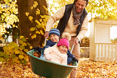 a father pushing his children through autumn leaves in a wheelbarrow