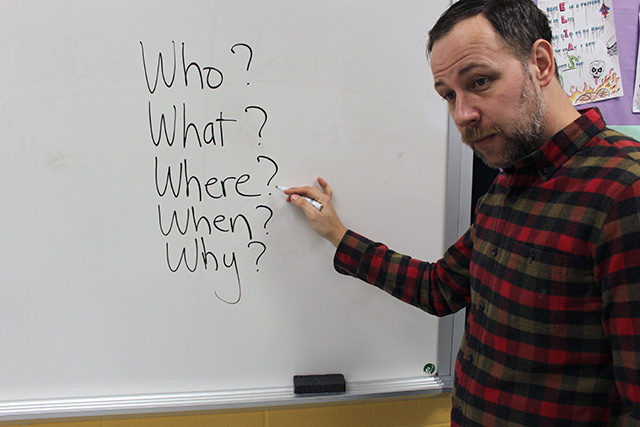 Mr. Lexington in front of a whiteboard on which is written 'who,'what,'when,'where,' and 'why'