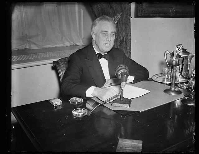 black and white photo of President Franklin Roosevelt sitting at a desk with microphones
