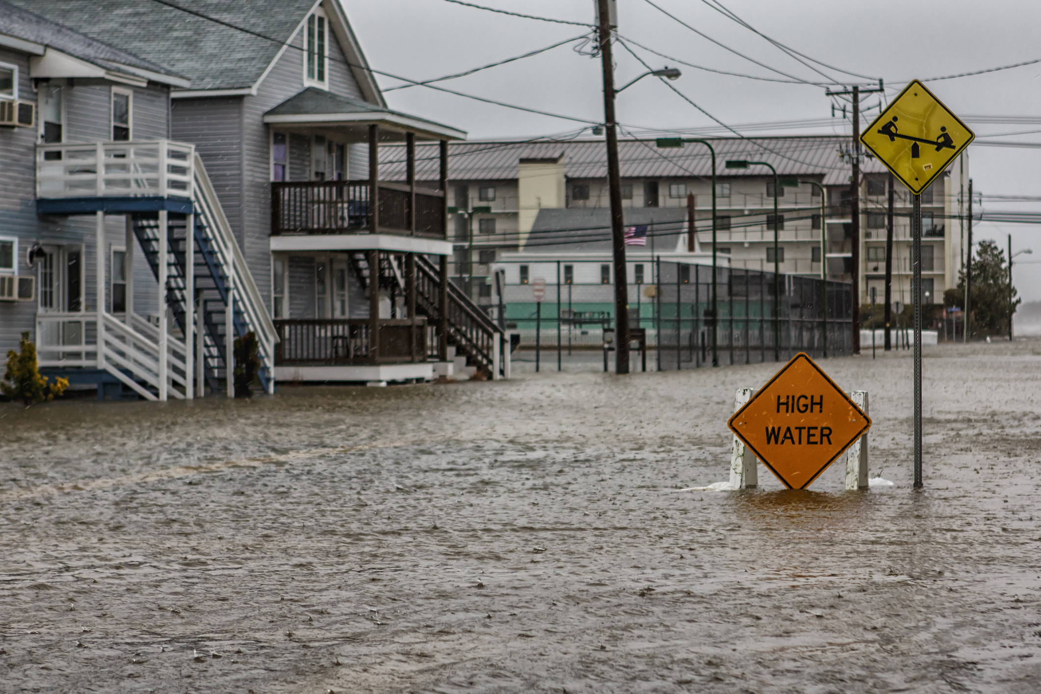 An oceanfront community street is flooded. The streets and sidewalks are not visible.
The high waters fill the first floor of some homes. A sign in the middle of the flood waters reads, “high waters.”